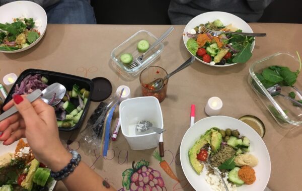 People eating salad in white bowls on a craft paper-covered table