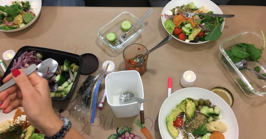 People eating salad in white bowls on a craft paper-covered table